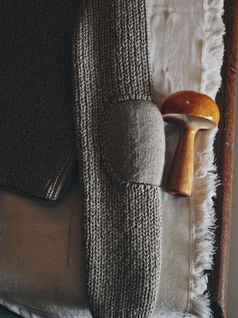 Illustration: ausgebesserter Strickpullover-Ellenbogen mit Stopfpilz und Nadel auf Leinen